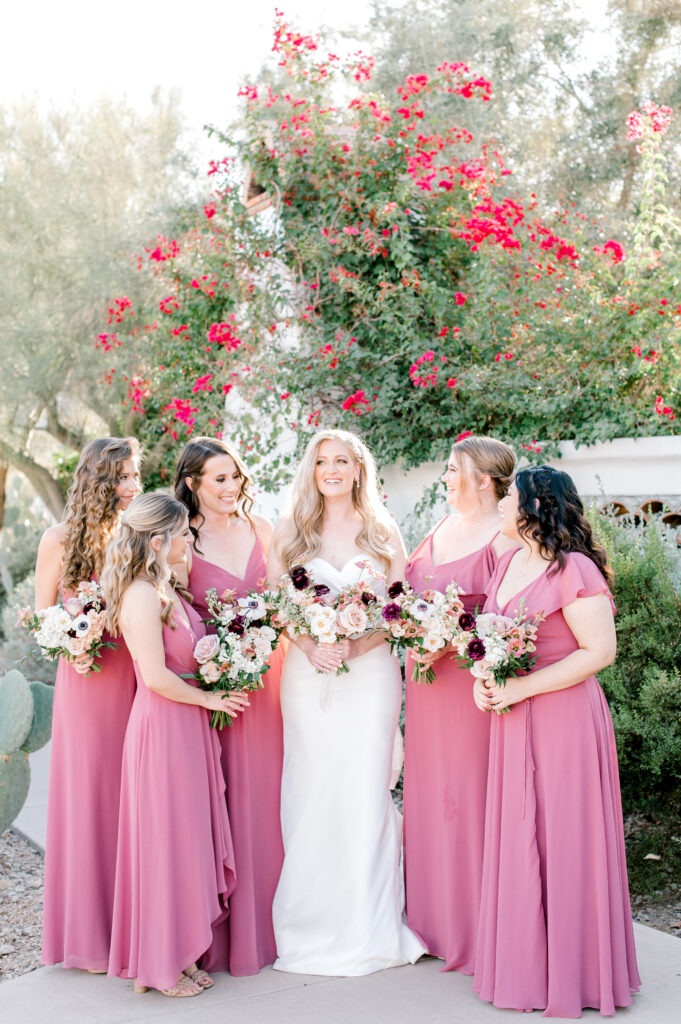 Bride standing in a group with bridesmaids in berry pink dresses, all holding bouquets.