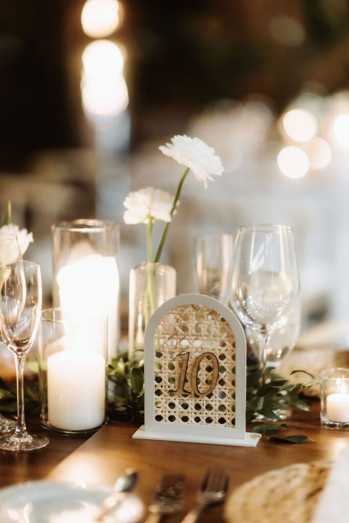 Lattice pattern table number sign with white flowers in a bud vase and candles on a table.