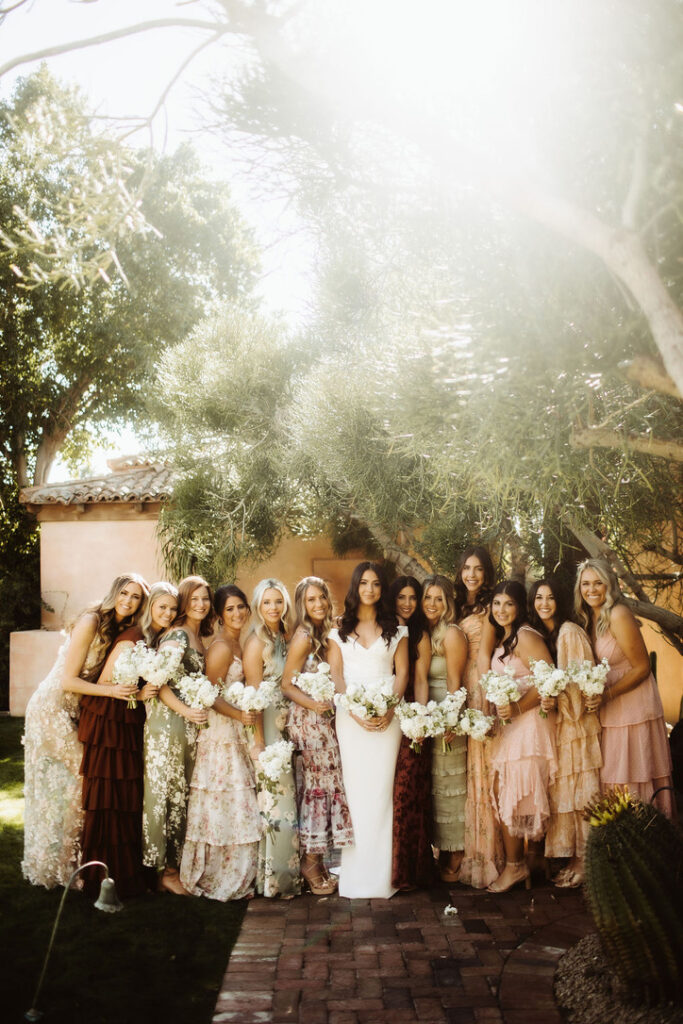 Bride standing in a row with bridesmaids in varied colors and patterns dresses.