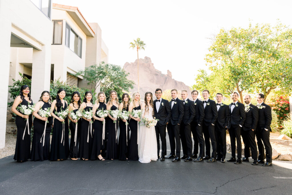 Wedding party in a line with bride and groom in center, bridesmaids and groomsmen in black with women holding bouquets.