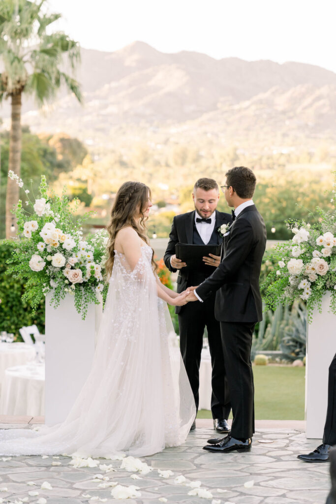 Bride and groom standing at front of outdoor ceremony altar space with officiant, mountain views in the distance.