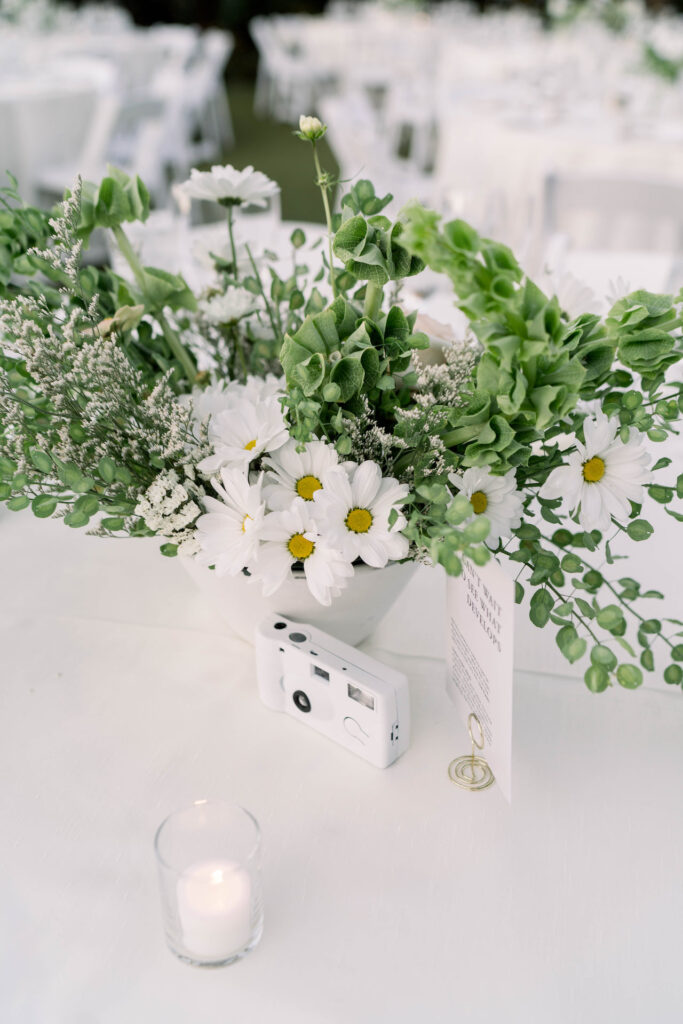 White floral and greenery centerpiece at wedding reception in a white vase.