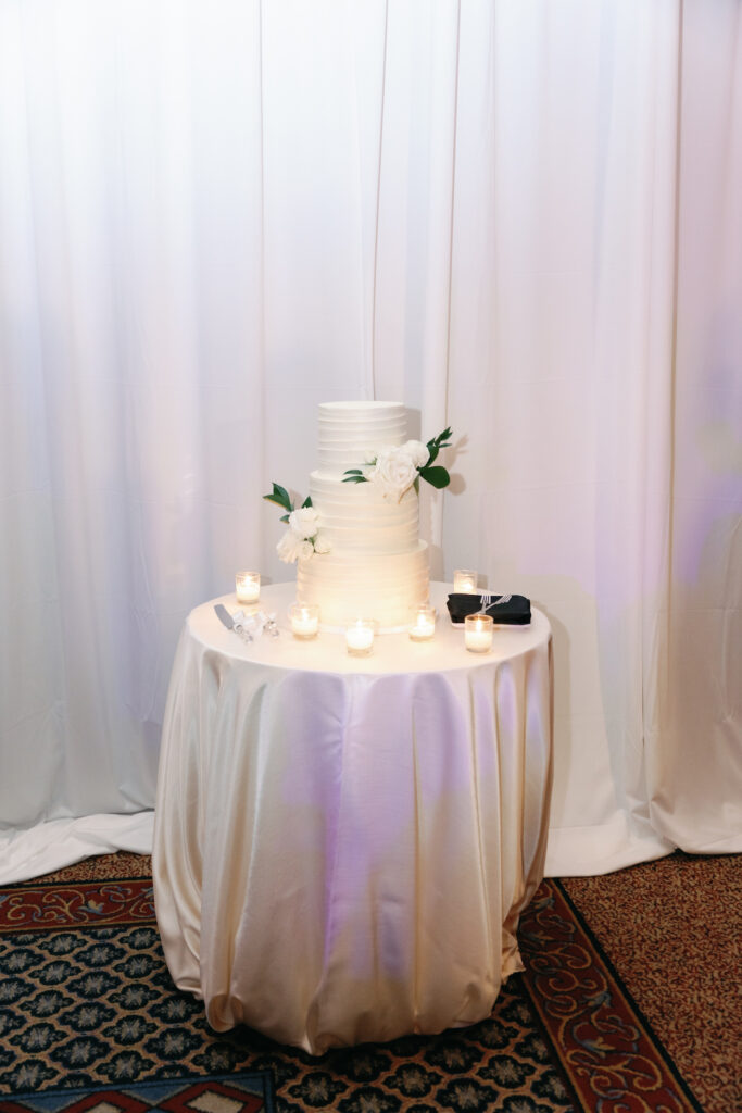 Three tiered white wedding cake with white roses added.
