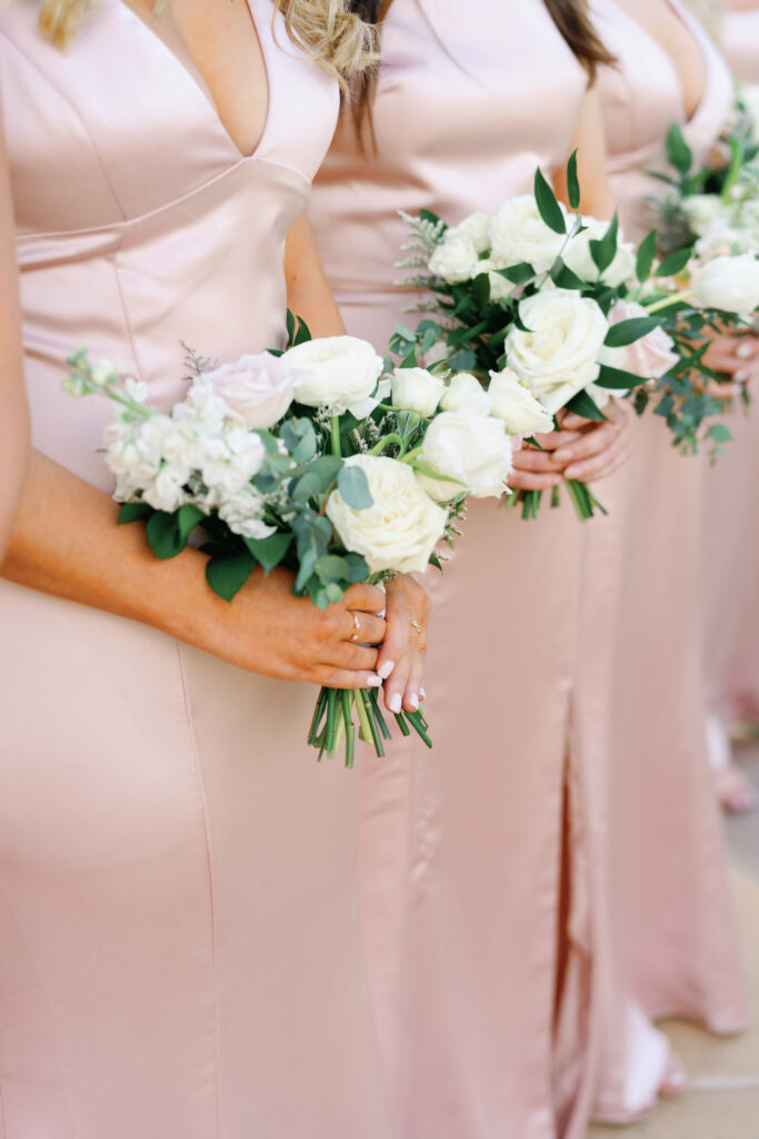 Bridesmaids in dusty pink dresses holding bouquet of white flowers.