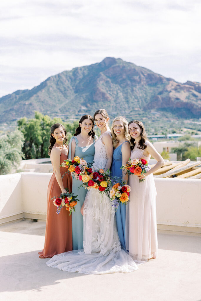 Bride standing outdoors with bridesmaids, all smiling and holding bouquets.