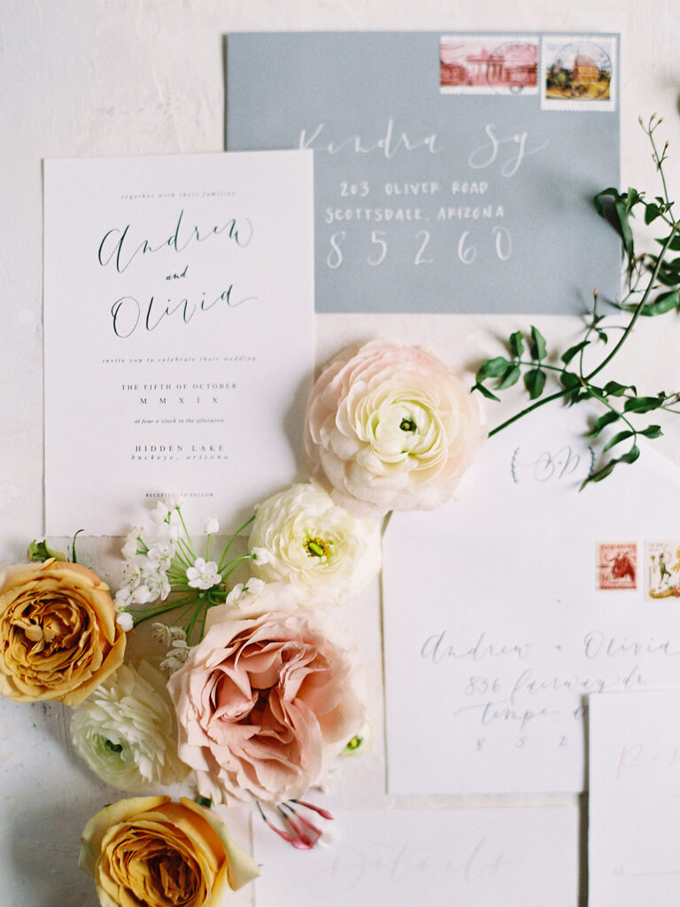 White invitation and gray envelope flat lay with flowers of white, pink, and yellow flowers.