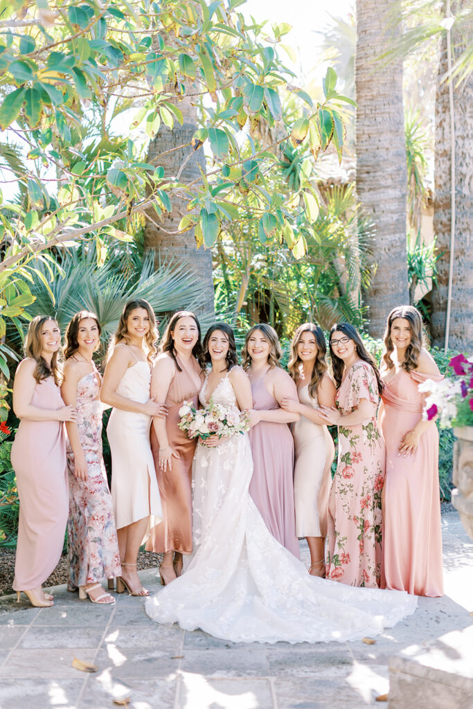 Bride standing with bridesmaids in a line all wearing blush shade dresses, some with patterns.