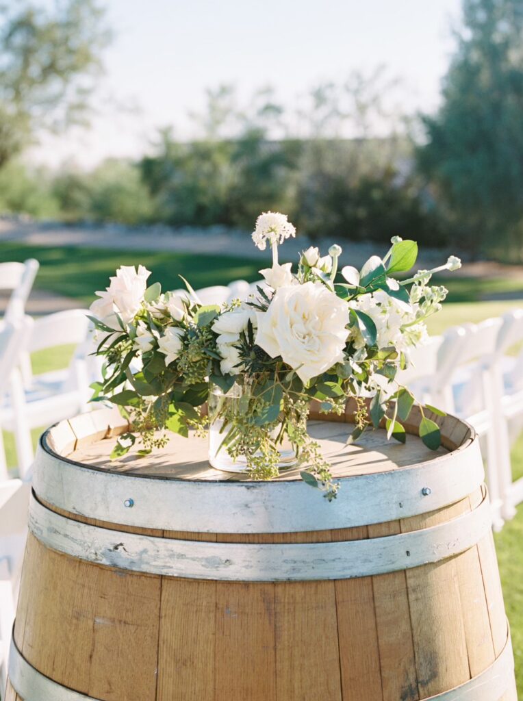 White and blush floral arrangement placed on top of wood barrel at wedding ceremoy.