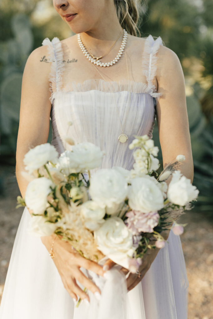 Bride looking down to side while holding bouquet or white and some light purple flowers.