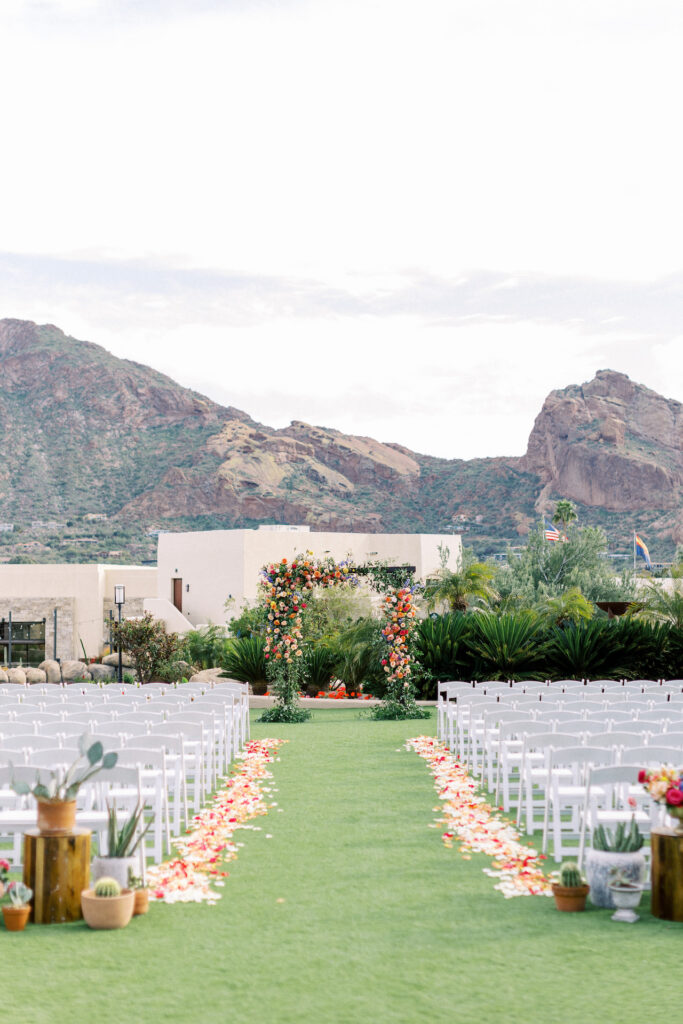 Outdoor wedding ceremony space at Camelback Inn with mountain views, a wedding arch with floral, rose petal lined aisle and back of aisle arrangements.