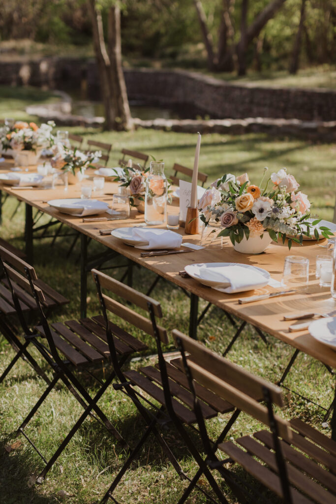 Long reception table outside in grass field with floral centerpieces down center.