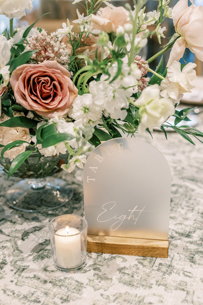 Frosted table number with floral centerpiece behind of white and blush floral and greenery.