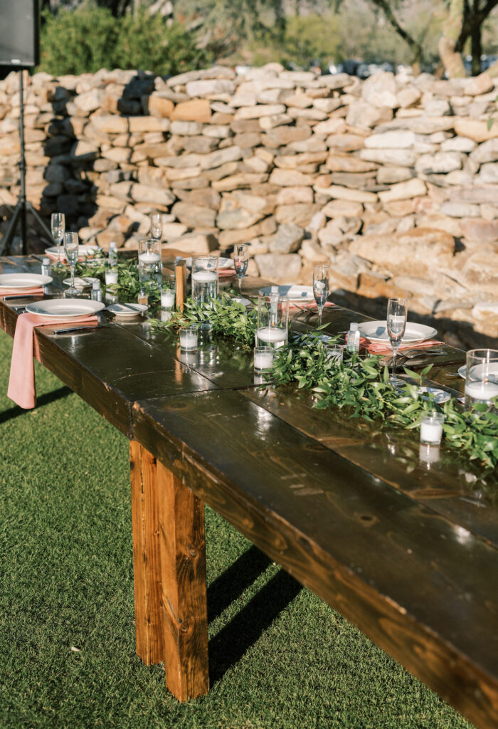 Long wood wedding reception table with greenery and candles down the center.