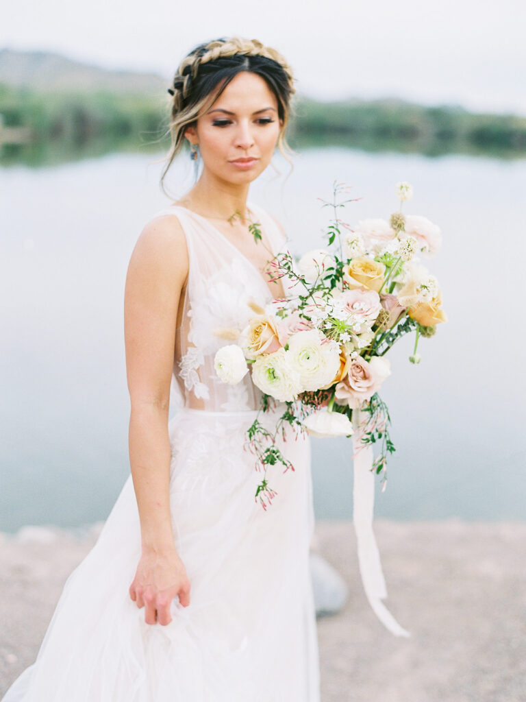 Bride looking down while holding bouquet of white, yellow and blush floral.