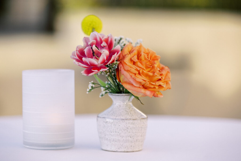 Pink, peach, and yellow flowers in a white ceramic bud vase next to a votive light.