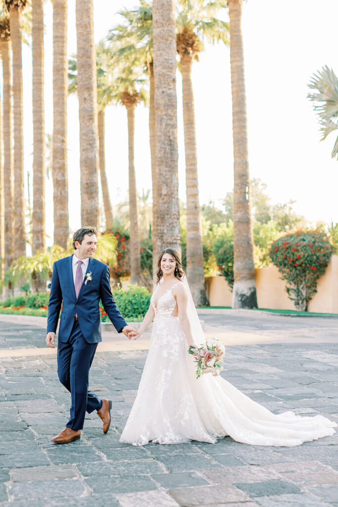 Bride and groom walking at Royal Palms on stone drive with palm trees in the background.