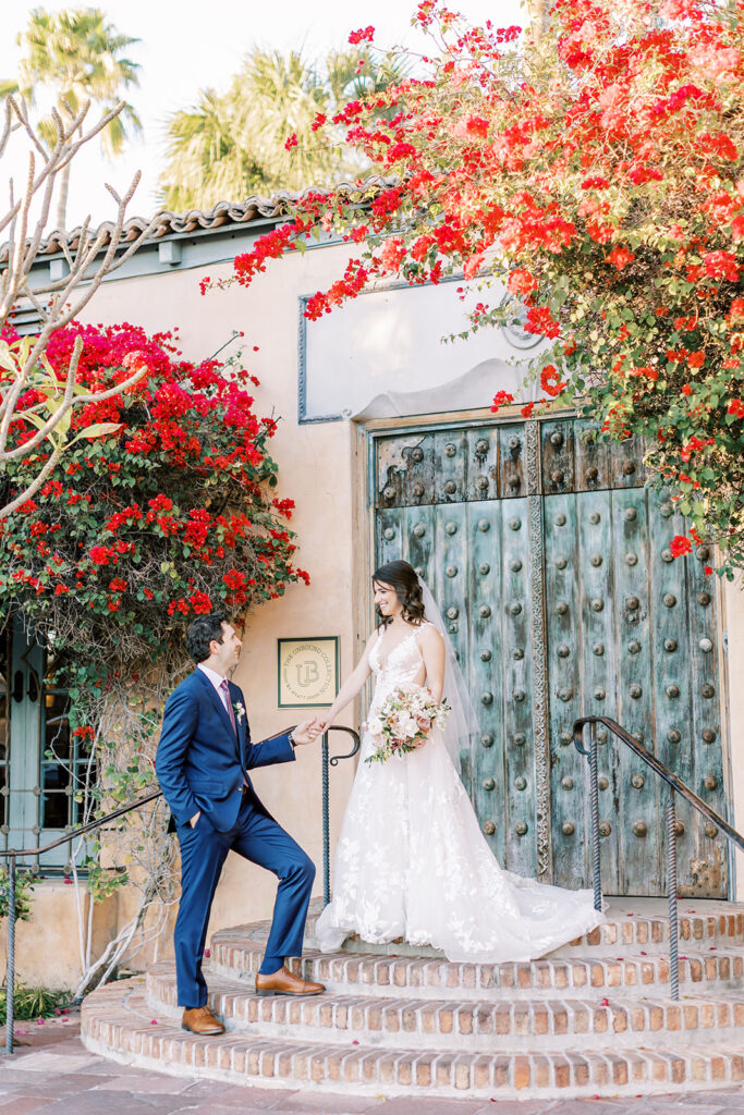 Groom holding bride's hand while she stands on top steps of Royal Palms entryway doors.