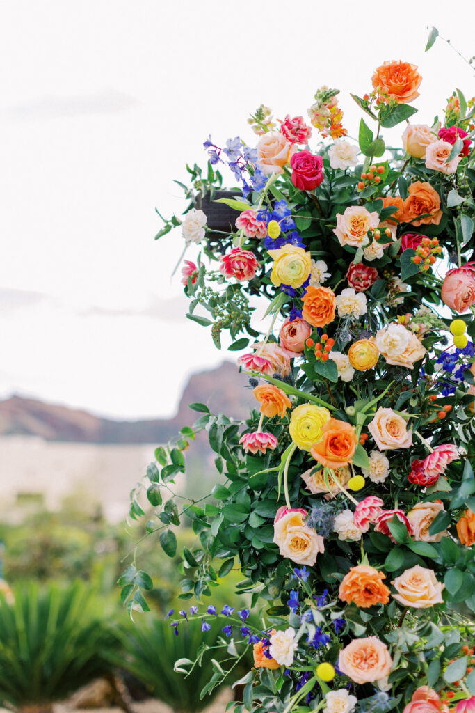 Wedding arch floral installation of greenery with vibrant colors including fuchsia, yellow, peach, purple, and blue.