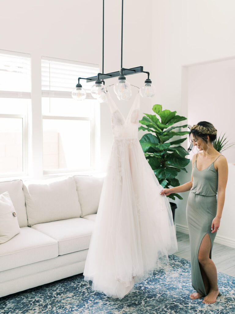 Bride holding out bridal gown hanging from modern light fixture in an indoor room.
