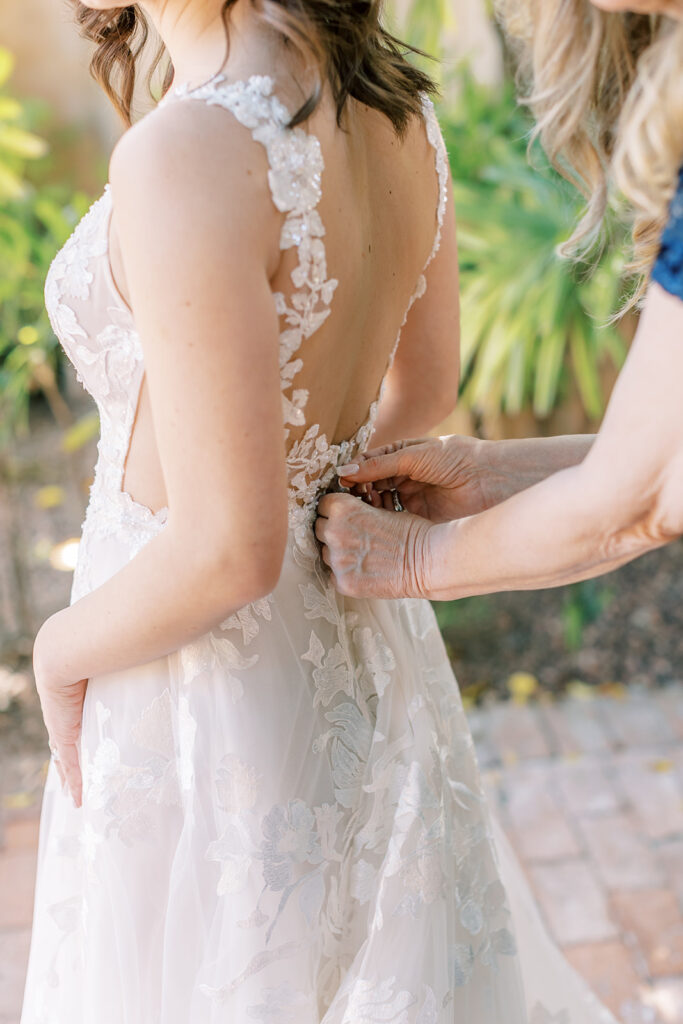 Bride receiving assistance with buttoning wedding dress.