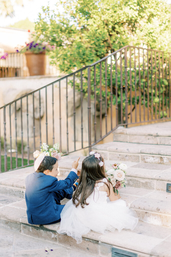 Flower girl and ring bearer boy sitting on step looking up steps.