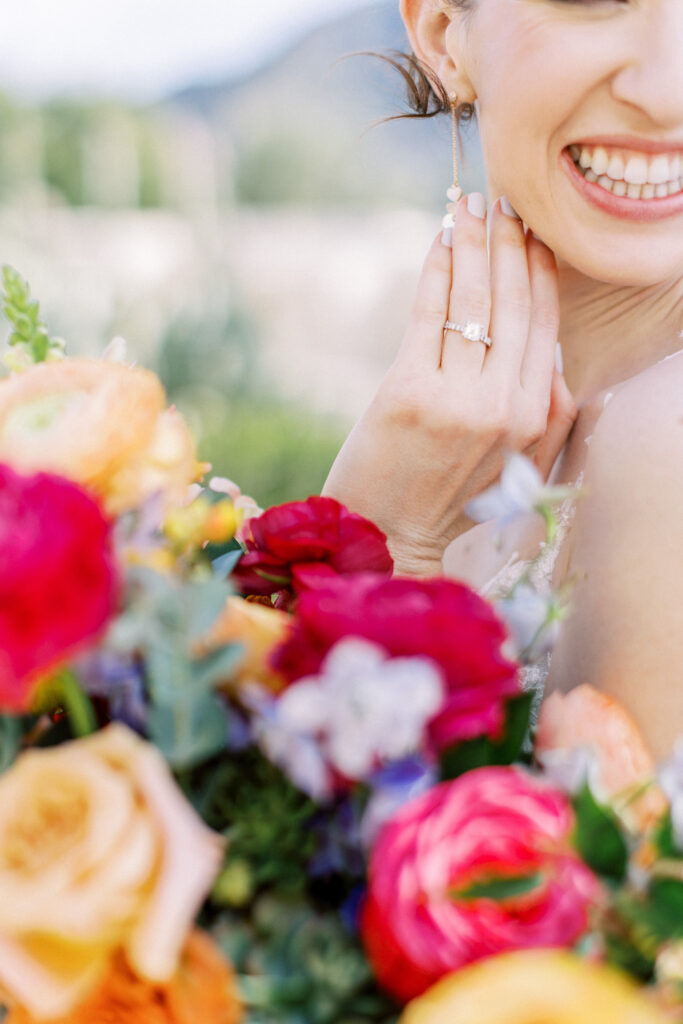 Smiling bride, holding hand up to her chin to show ring with bouquet flowers in bottom of picture.