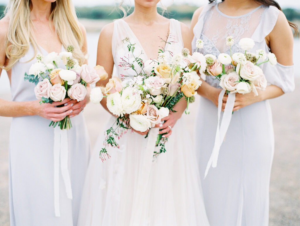 Bride and bridesmaids in light blue holding bouquets of white, yellow and blush floral.