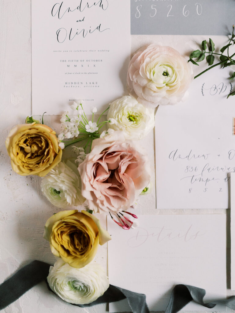 White invitation flat lay with flowers of white, pink, and yellow.