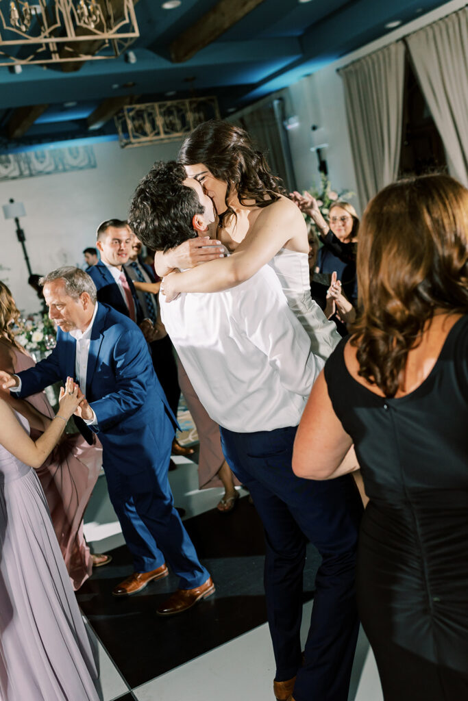 Groom lifting up bride and kissing each other on wedding reception dance floor.