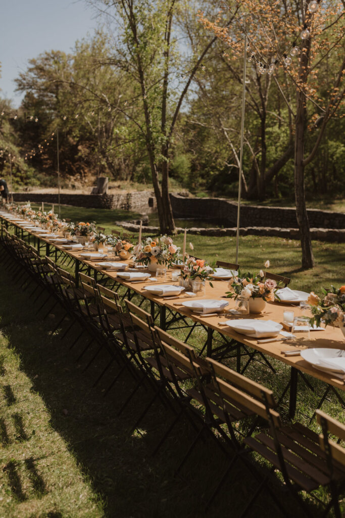 Long reception table outside in grass field with floral centerpieces down center.