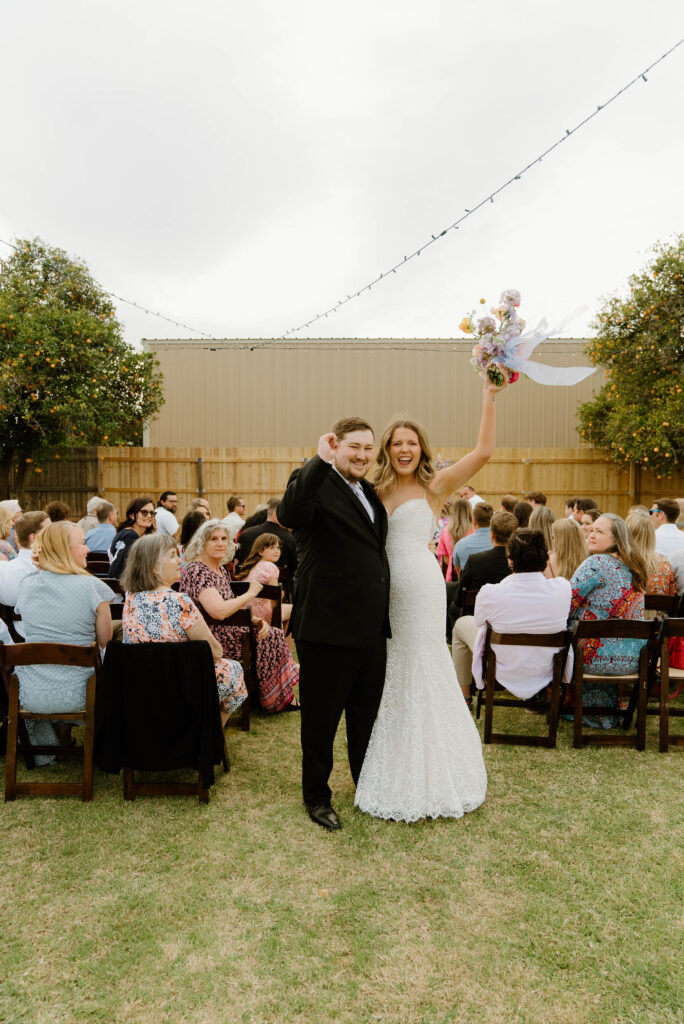 Bride and groom celebrating at back of ceremony aisle at outdoor backyard wedding.