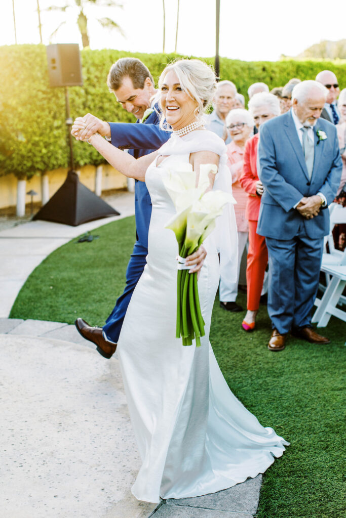 Bride and groom walking in ceremony aisle with arms raised in celebration.