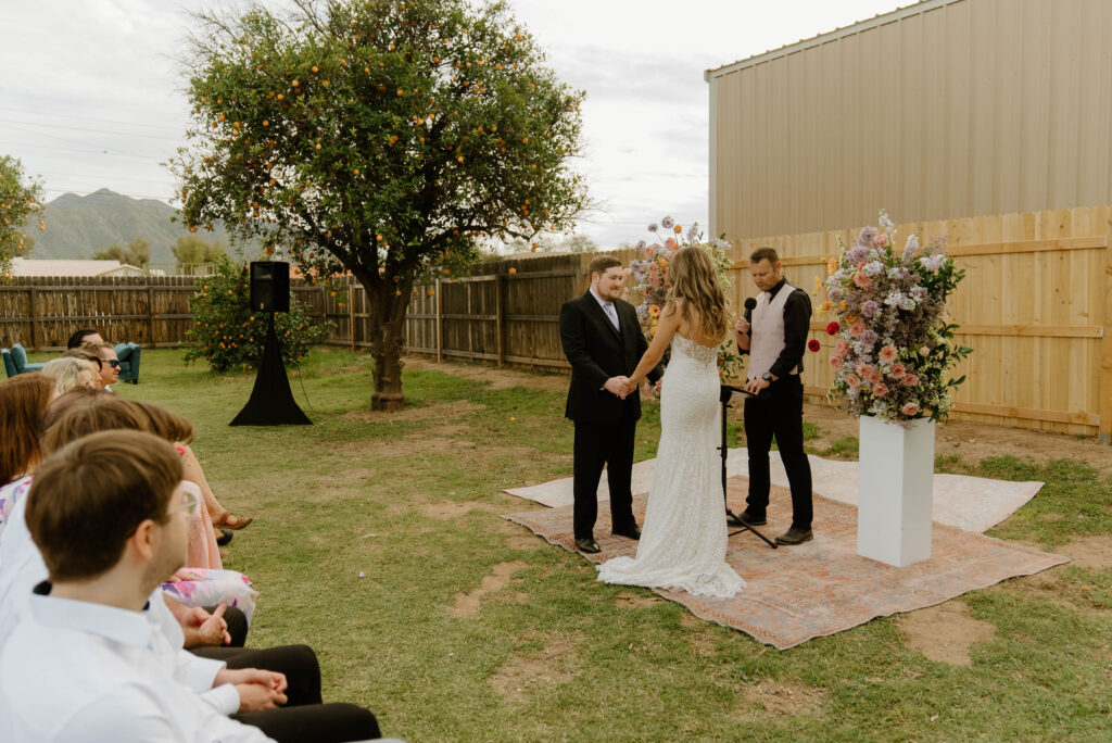 Bride and groom in altar space, standing between two floral columns with officiant during wedding ceremony.