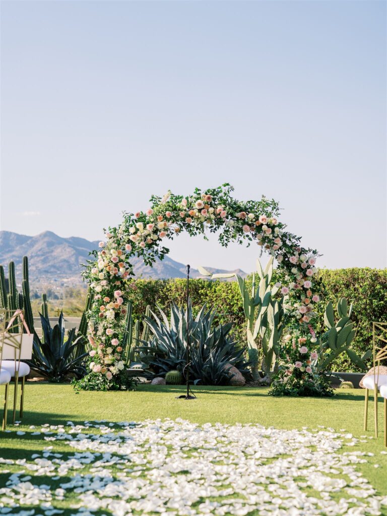Outdoor wedding ceremony arch of greenery and white, blush, pink, and mauve flowers.