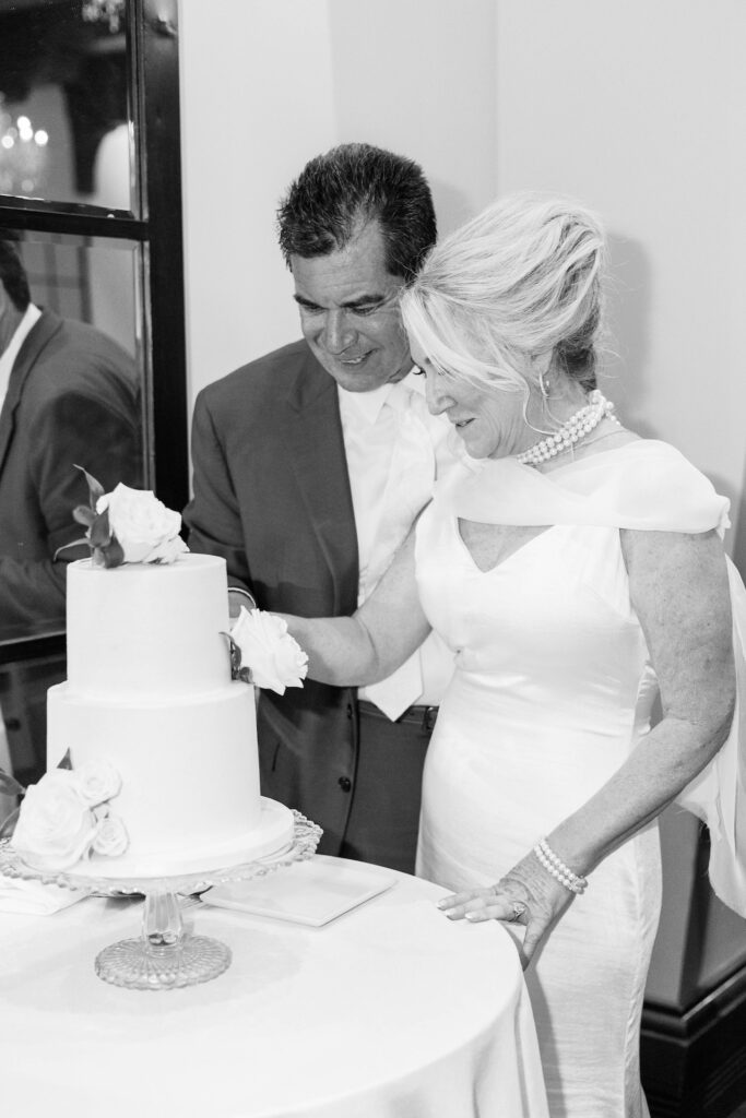 Bride and groom cutting two tiered cake, smiling.