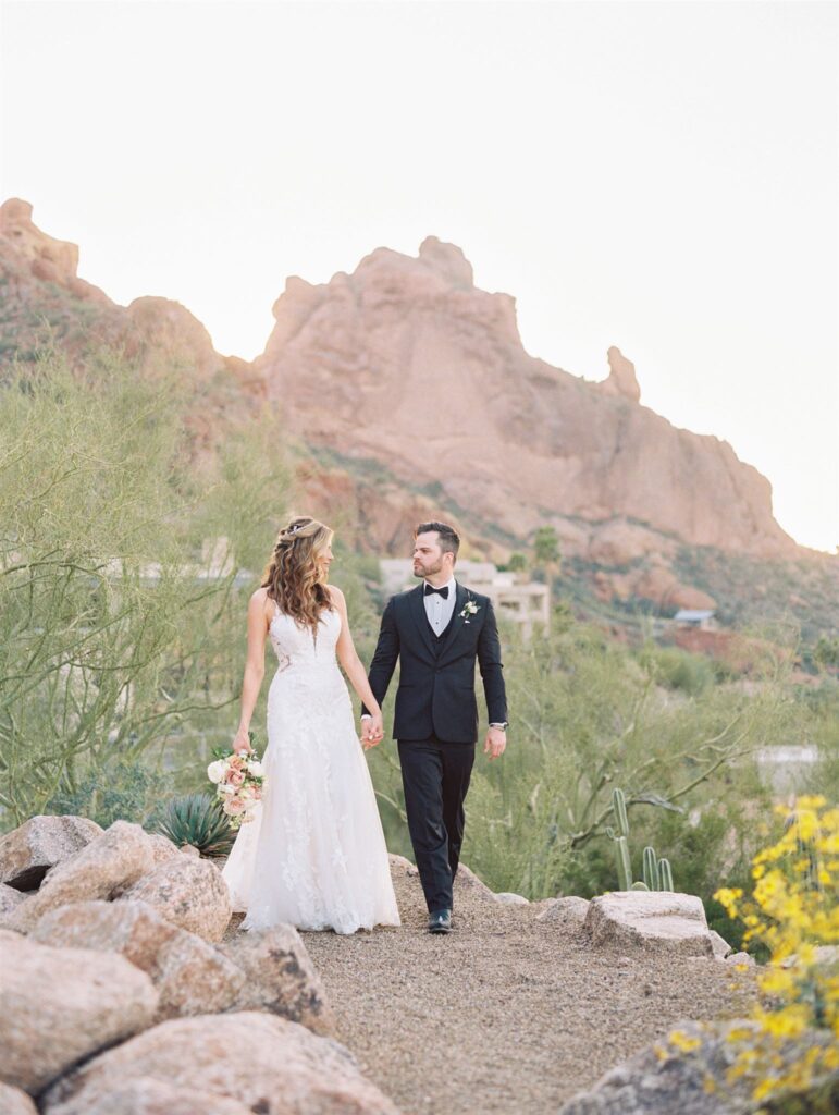 Bride and groom walking while holding hands in desert landscape.