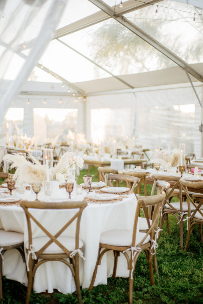 Tent reception space with rectangle and round reception tables with roses and pampas centerpieces.