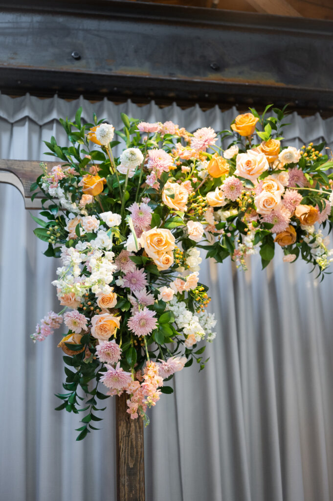 Wedding ceremony arch floral installation of greenery, pink, white, and yellow flowers.