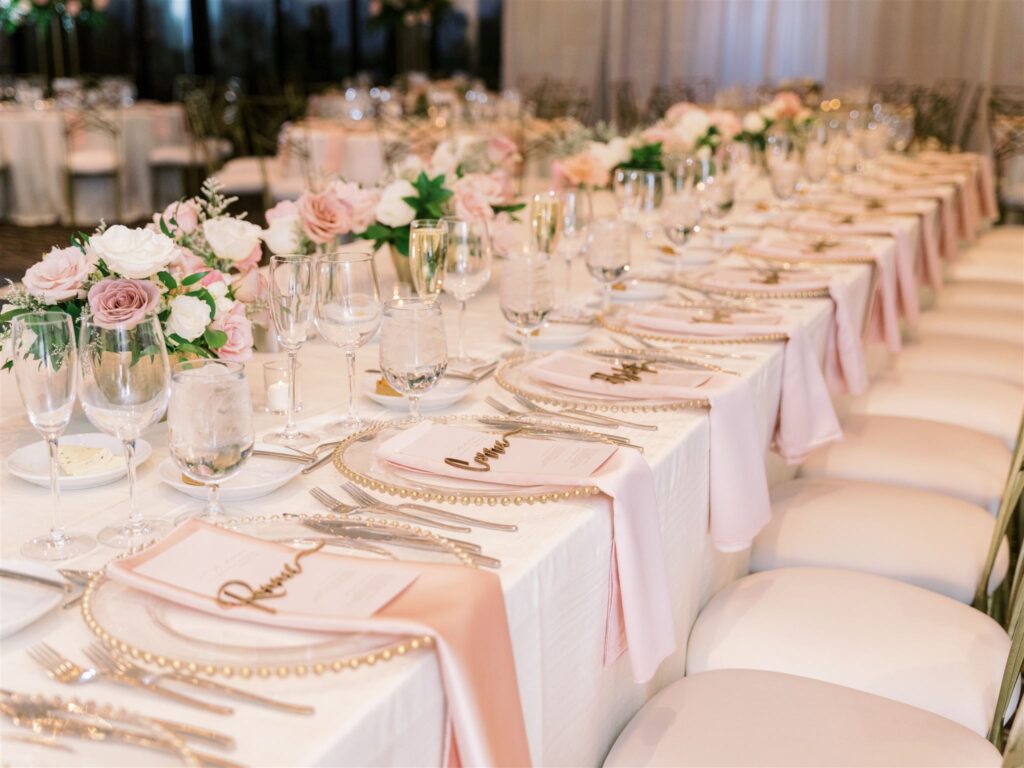 Long reception table of centerpieces of white and pink flowers, white and pink linens and pearl studded plates.