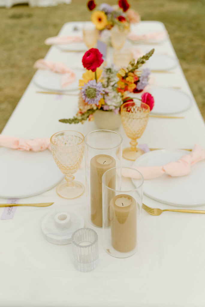 Table at wedding reception with white plates and pink napkins place setting with floral centerpieces.
