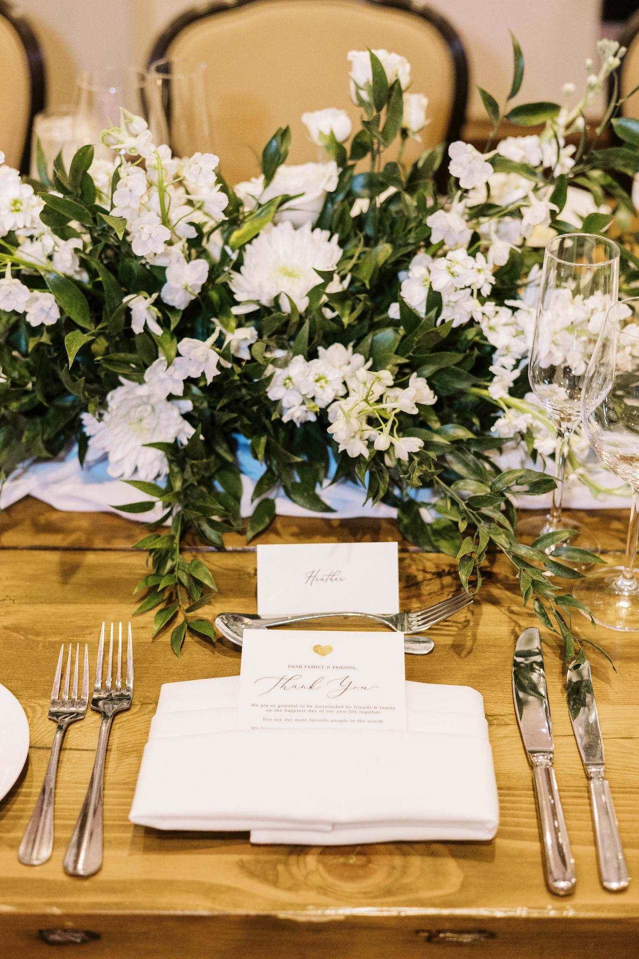 Wedding reception place setting with lush white flowers and greenery centerpiece.