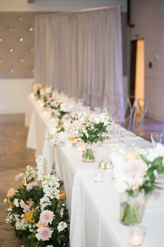 Long reception head table with floral and votive candles down the front part of the table.