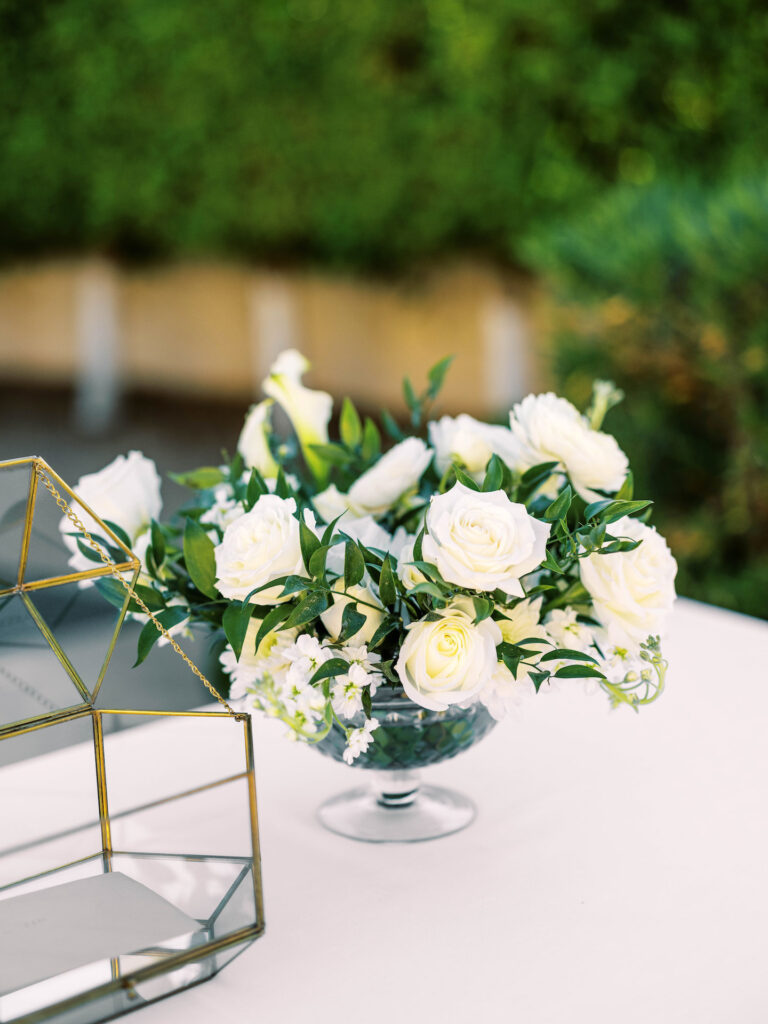 Large wedding reception centerpiece of white flowers and greenery in a glass vase.