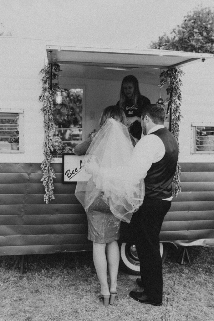 Bride and groom visiting mobile bar from in camper at wedding.