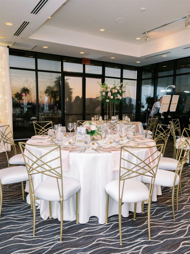 Round reception tables at indoor wedding reception at Sanctuary resort with white linens and white and pink low and tall floral arrangements.