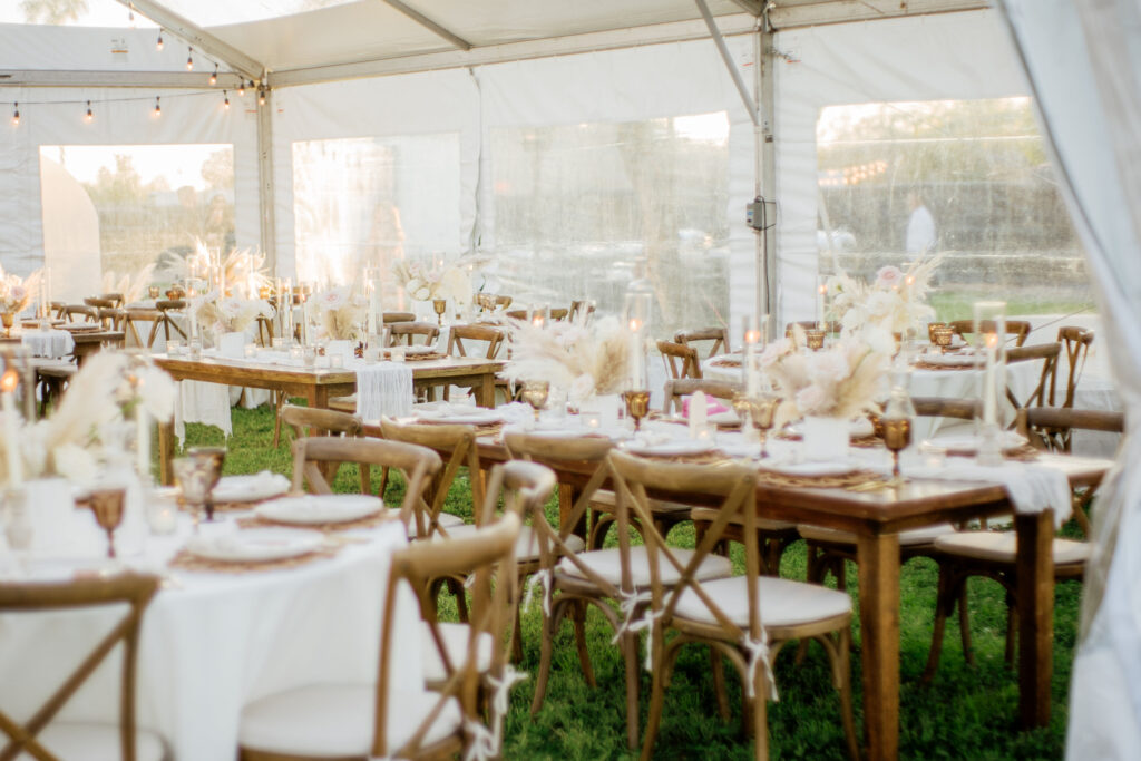 Tent reception space with rectangle and round reception tables with roses and pampas centerpieces.