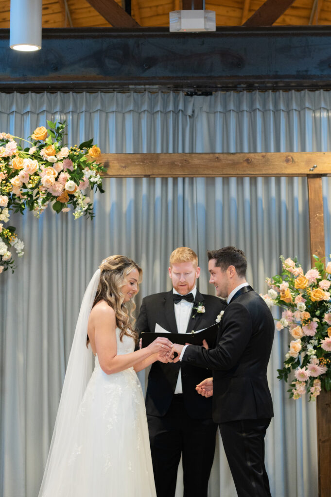 Bride and groom at wedding ceremony altar with officiant, exchanging rings.