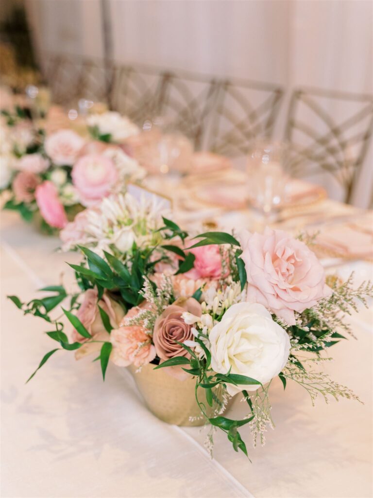 Low wedding reception centerpieces of white, blush, pink, and mauve flowers in gold vase.