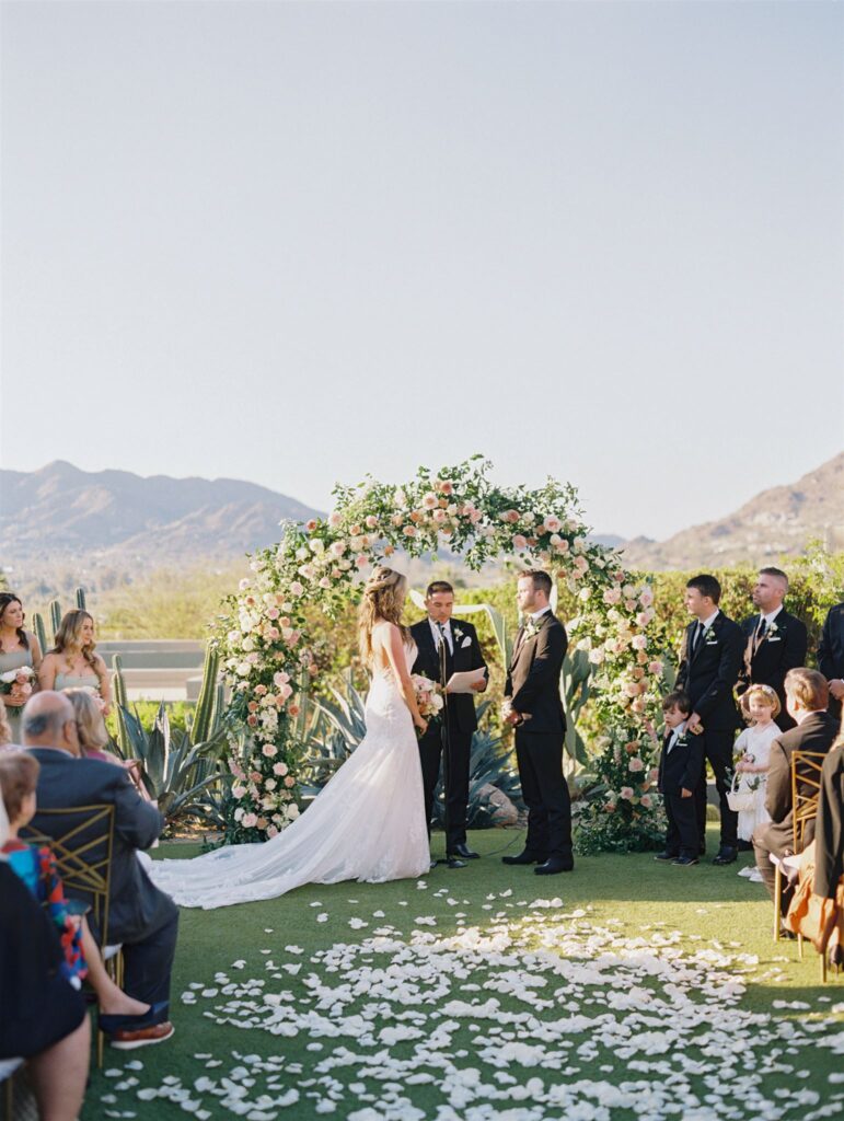 Outdoor wedding ceremony at Sanctuary resort with white rose petals in aisle and bride and groom standing in front of arch with officiant.