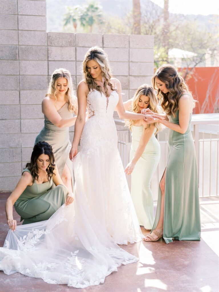 Bridesmaids helping bride get ready in wedding gown. Bridesmaids wearing mint green shade dresses.